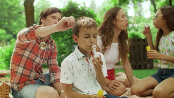 Дівчинка і хлопчик грають з мильними бульбашками в парку. Сім'я має пікнік у лісі — стокове фото