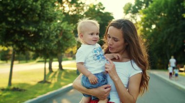 Anne, çocuğu parkta elinde tutuyor. Kadın ve çocuk dışarıda birlikte oynuyorlar.