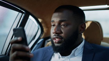 Afrikalı iş adamı araçta akıllı telefon kullanıyor. Üzgün afro adam gözlerini ovuyor.
