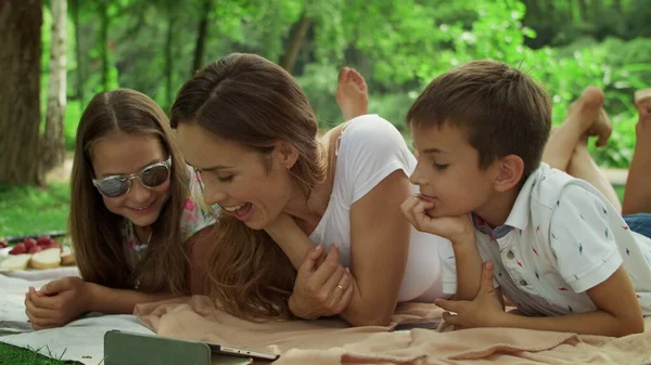 Crianças felizes com a mãe usando tablet digital no parque de verão — Fotografia de Stock