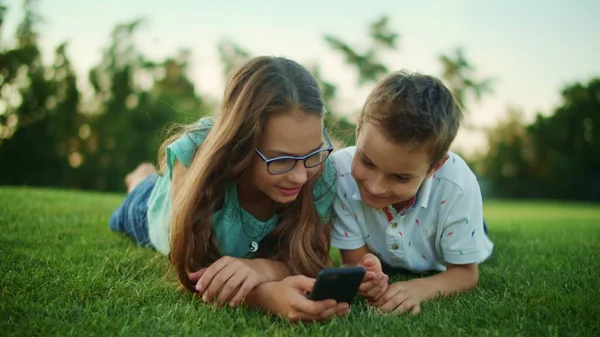 Pojke och flicka ligger på gräs med mobiltelefon. Broder och syster använder smartphone — Stockfoto