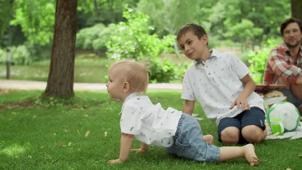 Liebenswertes Kleinkind, das im Park auf Gras fällt. Eltern lachen mit Kindern im Freien — Stockfoto