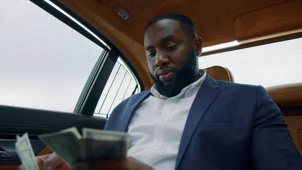 Portrait of businessman counting money at car. African guy smelling money at car