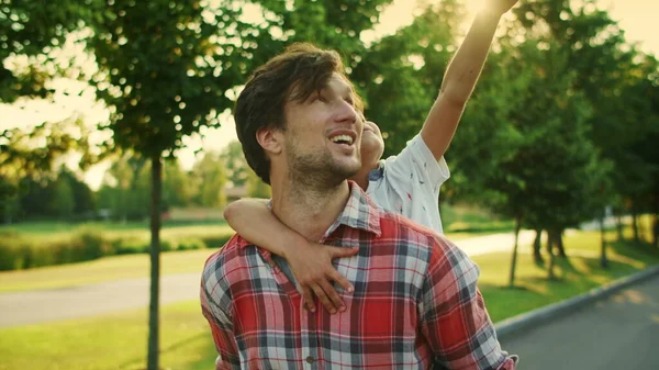 Pai e filho andando na rua. Sorrindo homem carregando menino de volta no parque — Fotografia de Stock
