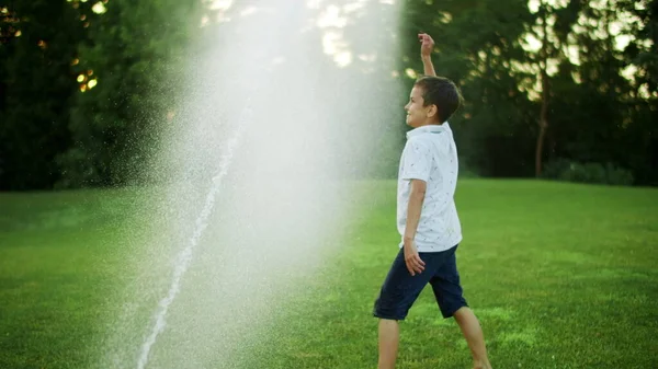 Positiver Junge steht auf der Wiese. Kind spielt mit Wassersprenger auf Feld — Stockfoto