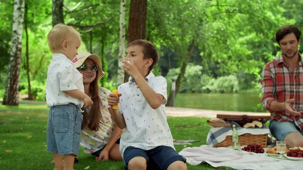 Children having fun with soap bubbles in park. Parents talking together outdoors — Stock Photo, Image