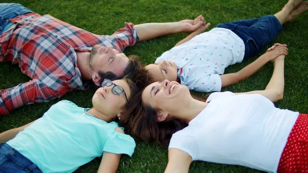 Семья лежала в кругу на траве. Родители и дети держатся за руки — стоковое фото