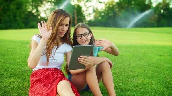 Cute girl and woman waving hands at camera on digital tablet outdoors