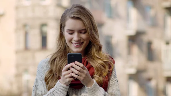 Mulher feliz enviando mensagens por telefone ao ar livre. Sorrindo menina recebendo mensagem na rua — Fotografia de Stock