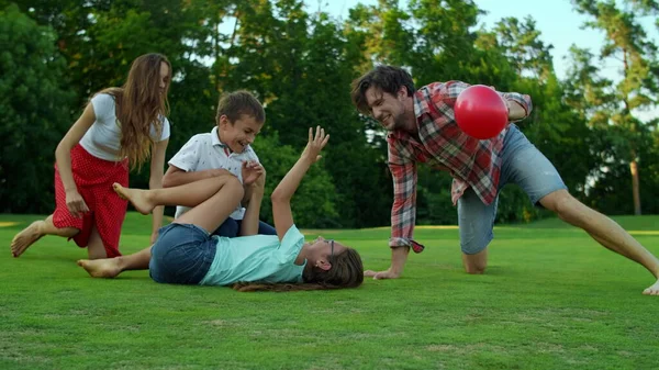 Flicka liggande på gräs med boll på plan. Ung familj leker med bollen på ängen — Stockfoto