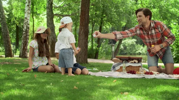 Positive parents blowing soap bubbles with children in park — Stock Photo, Image