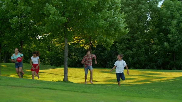 Familie läuft auf der grünen Wiese. Eltern und Kinder spielen im Freien mit Ball — Stockfoto