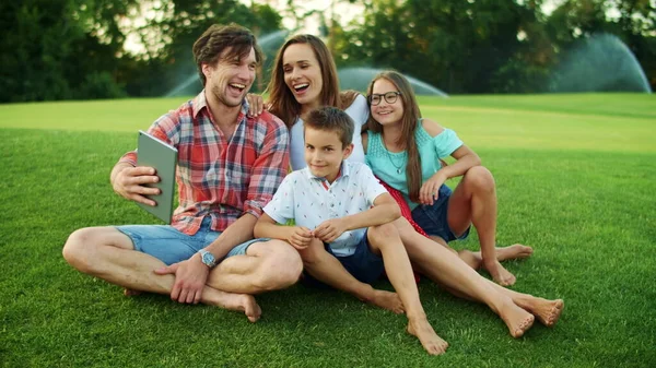 Семья смеется вместе в парке. Семья проводит видео-чат на лугу — стоковое фото
