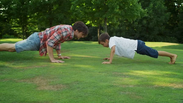 Rapaz e homem em posição de prancha. Pai e filho fazendo flexões no parque — Fotografia de Stock