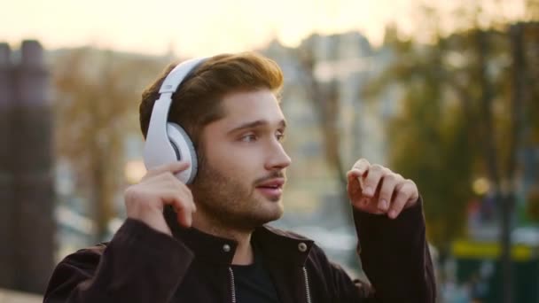 Homem emocional ouvindo fones de ouvido de música lá fora. Cara animado cantando na caminhada — Vídeo de Stock