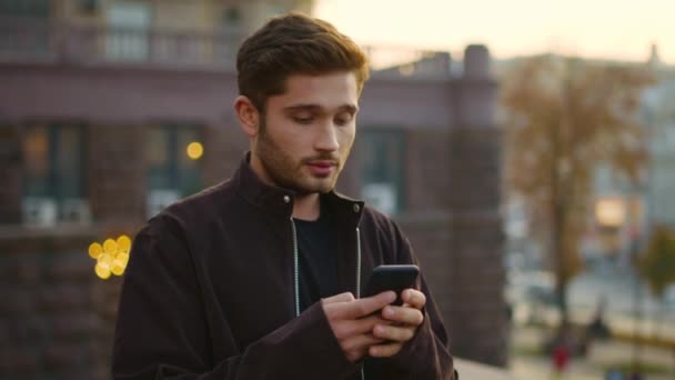 Glad man som tittar på telefonskärmen på gatan. Leende kille chattar via telefon utomhus. — Stockvideo