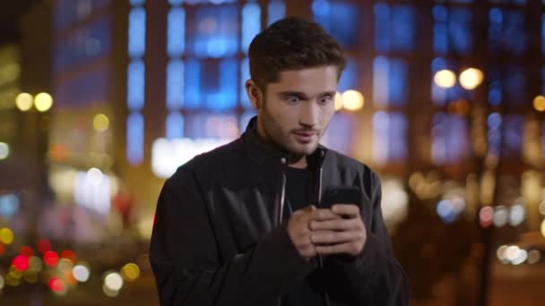 Verrassende man die buiten sms 'jes leest. Happy guy op zoek telefoon scherm — Stockvideo