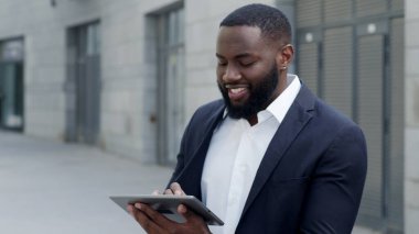 Afro işadamı sokaktaki tablete mesaj yazıyor. İşçi dışarıda ped kullanıyor.