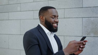 Gülümseyen iş adamı sokakta akıllı telefon kullanıyor. Şehirde yürüyen bir iş adamı