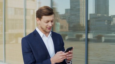 İş adamı sokakta cep telefonuyla yazı yazıyor. Çalışan kaldırımda iş arıyor.