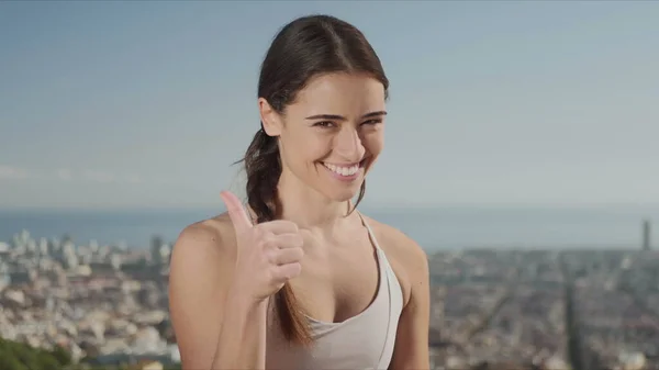 Deportiva mostrando un cartel con los pulgares arriba. Mujer de fitness mirando la cámara exterior —  Fotos de Stock