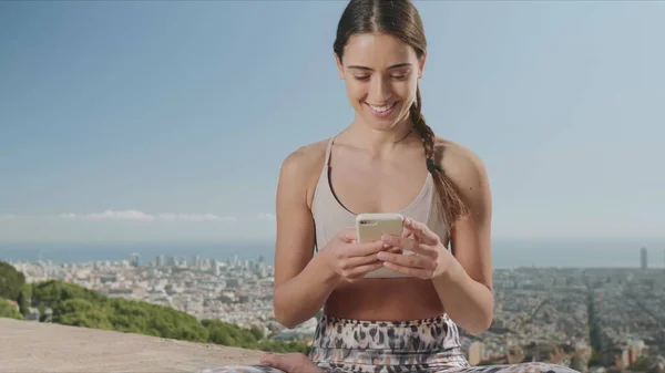 Mujer sentada en pose de loto con smartphone. Chica usando el teléfono celular en la ciudad — Foto de Stock