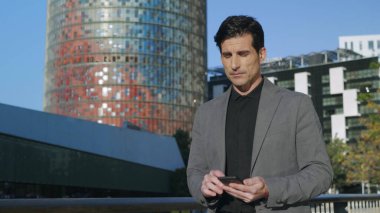 İş adamı dışarıda cep telefonuyla yazı yazıyor. Sokakta yürüyen odaklı bir çalışan