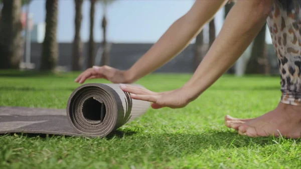 Жінка рухається вгору йога килимок після тренування в парку. Дівчина складаний килимок на траві — стокове фото