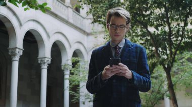 Öğrenci üniversitenin bölgesinde telefonla internette geziniyor. Akıllı telefon kullanan adam.