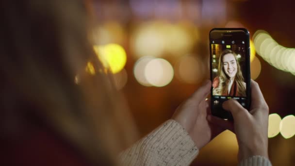 Widok z tyłu dziewczyna robi selfie telefon na ciemnej ulicy. Kobieta trzyma telefon komórkowy. — Wideo stockowe
