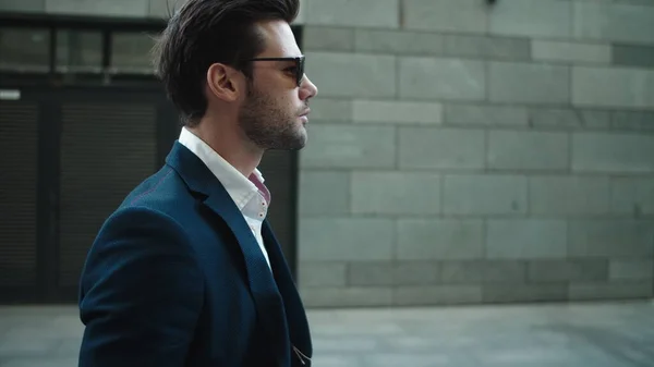 Side view businessman walking in suit. Man wearing sunglasses at street
