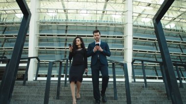 Cep telefonlarıyla yürüyen bir çift. Sokakta birlikte akıllı telefon kullanan çift.