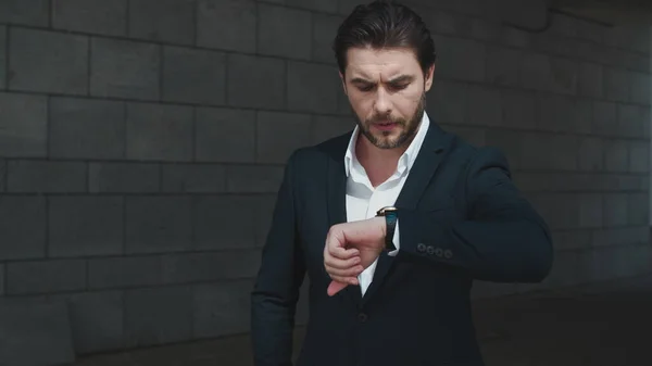 Worried business man checking time on wristwatch in modern city