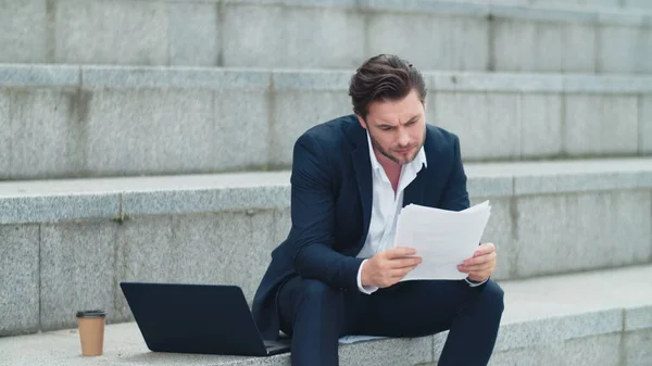 Businessman thinking about financial documents on street. Man reading documents