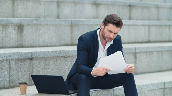 Businessman reading business papers on street. Man sitting on stairs — Stock Photo, Image