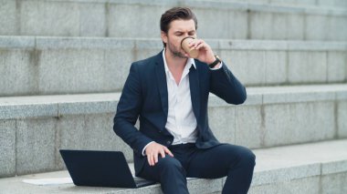 Sokakta dizüstü bilgisayarda daktilo yazan bir iş adamı. İçen adam kahveyi götürür.