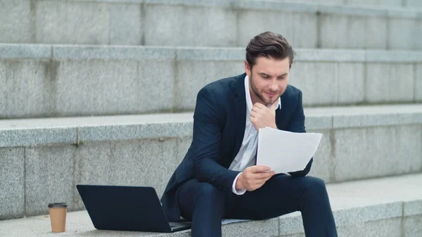 Business man looking at papers on street. Executive thinking about graphs