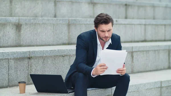 Businessman reading business papers on street. Worried man sitting on stairs — Stock Photo, Image