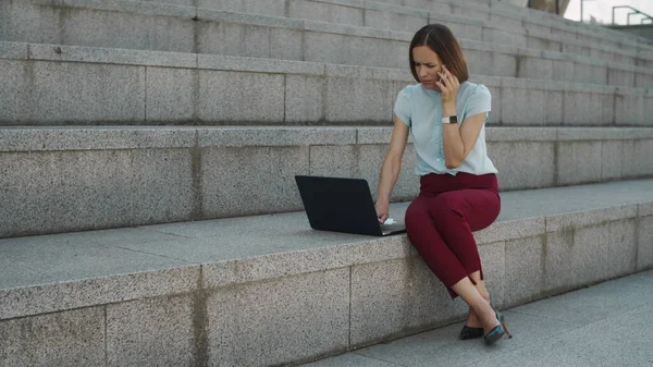 Geschäftsfrau spricht draußen auf dem Smartphone. Frau arbeitet am Laptop — Stockfoto