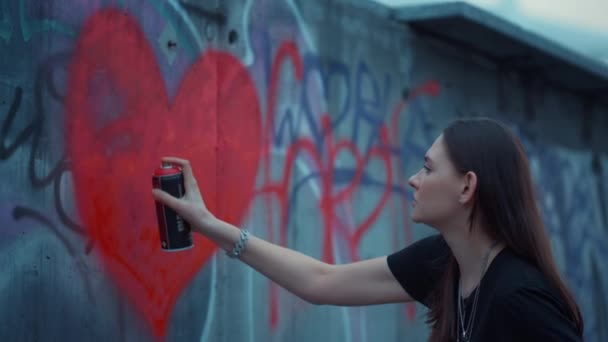 Een meisje dat graffiti op de muur tekent. Gericht vrouw schilderen hart met spray fles — Stockvideo