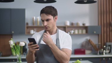 Gülümseyen şefin portresi ev mutfağında cep telefonundan tarifi arıyor..