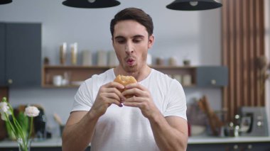 Ev mutfağında hamburger yiyen aç bir adam. Aç adam çizburgerin tadını çıkarıyor.