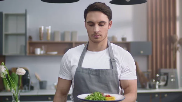 Han lager mat og lukter salat på kjøkkenet. Munter kokk med sunn mat – stockfoto