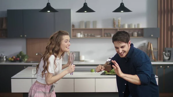 Cheerful couple singing song in kitchenware at home kitchen. Friends having fun