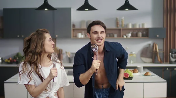 Pareja divertida cantando en cuchara y bigote en la cocina moderna en cámara lenta . — Foto de Stock