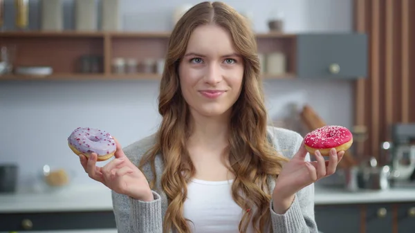 Smiling woman choosing between two donuts at home. Girl having fun with cakes.