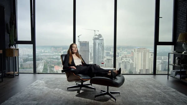 Businesswoman relaxing on chair in modern interior. Serious manager looking away