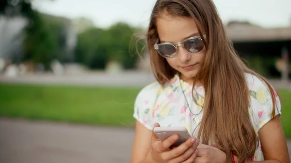 Mosolygó lány játszik a mobiltelefon a szabadban. Lány áll a parkban — Stock Fotó