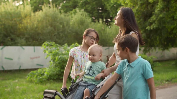 Avslappnad mor promenader med tre barn. Glad familj avkopplande i sommarparken — Stockfoto