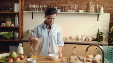 Kadın mutfakta mısır gevreği kasesi hazırlıyor. Esmer, kaseye mısır gevreği dolduruyor..